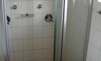 A simple bathroom with a shower and gray tiles. The shower has two showerheads and a glass partition.