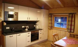 A modern kitchen with wood details and white cabinets. There is a dining table and windows with checked curtains.
