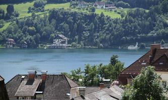 A quiet lake overlooking green hills and charming houses. The roofs of the surrounding buildings are visible in the foreground.