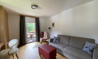 A cozy living room with a gray sofa and a red ottoman. There is access to the balcony with a view of the greenery.