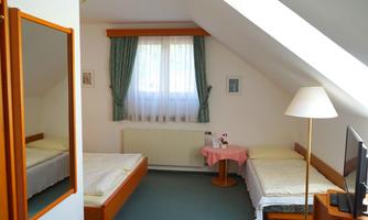 A simple room in the attic with two single beds, a table, and a television. Bright walls and a window provide plenty of daylight.
