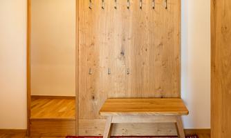 A simple entrance area with a wooden bench and a wooden coat rack. The floor is made of light wood and a colorful rug lies next to it.