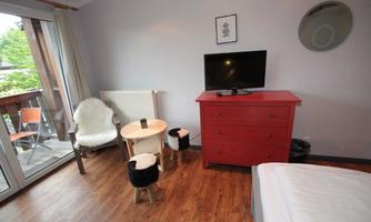 A cozy room with wooden floors, a television, and a red cabinet. A small table and a comfortable chair complete the furnishings.