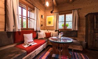 A cozy living area with wooden walls and a round table. The seating area is decorated with colorful cushions and a rug.