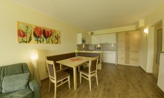A bright living space with a modern kitchen and a dining area. A painting with colorful tulips hangs on the wall.