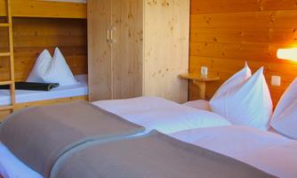 A cozy hotel room with wooden paneling. There is a double bed and a bunk bed for extra space.