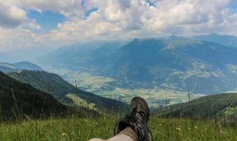 A person is lying in the grass and looking at an impressive mountain landscape. In the background, there are green hills and a blue sky with clouds.