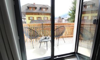 A balcony with two chairs and a small table. In the background, colorful houses and trees are visible.