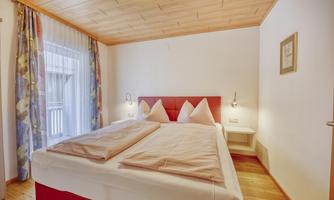 A cozy bedroom with a double bed and two pillows. Large windows let in plenty of light and provide a view outside.