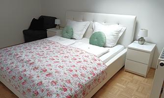 A modern bedroom with a white bed and a floral comforter. Next to the bed are nightstands with lamps.
