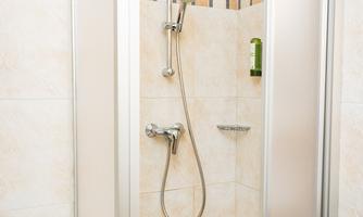 A modern shower with transparent glass doors is located in a bright bathroom. The walls are adorned with warm tiles and decorative mosaics.