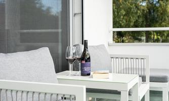 A cozy terrace with two modern chairs and a small table. On the table are wine glasses and a bottle of wine.