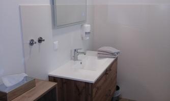 A modern bathroom with a wooden vanity and a large mirror. The walls are light, and towels are neatly arranged.
