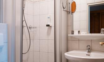 A modern bathroom with a shower stall and a small sink. The walls are designed with white tiles.