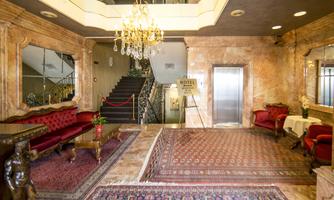 An elegant reception area with red sofas and a carpet. A crystal chandelier hangs above the room and a staircase leads upstairs.