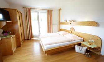 A bright bedroom with a double bed and wooden furniture. Large windows provide plenty of natural light and a pleasant living space.