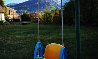 A colorful swing stands in a garden with a view of the mountains. The sky is blue and the landscape is green and inviting.
