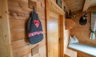 A cozy room with wooden walls and a small window. A gray bag with a red heart is hanging on the wall.
