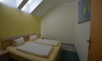 A simple bedroom with two beds and a window with a sloping roof. The walls are painted yellow and the room feels bright and welcoming.