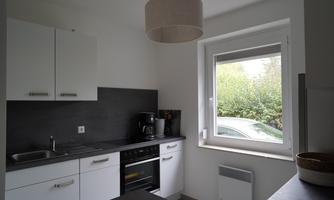 A modern kitchen with white cabinets and a dark countertop. A window offers a view of the greenery.