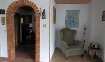 An inviting living area with a green armchair and an archway made of red bricks. A colorful picture hangs on the wall, and the floor is made of light wood.