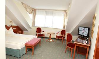 A cozy room with a double bed and a table with chairs. Large windows provide plenty of daylight.
