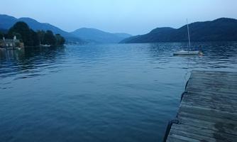 A quiet lake with gentle hills in the background. A boat is docked at the pier and dusk is setting in.