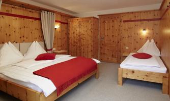 A cozy room with wood paneling, a double bed, and a single bed. The decor is simple and modern, with red accents.
