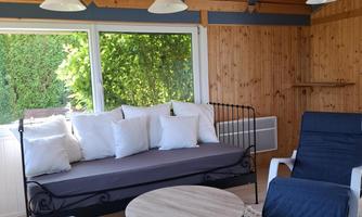 A cozy room with a sofa bed, two armchairs, and a round table. Large windows let in plenty of daylight and offer a view of the greenery.