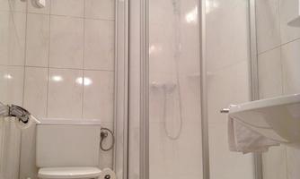 A simple bathroom with a shower, toilet, and sink. The walls are tiled and the fittings are modern.