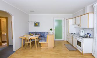 A bright, modern kitchen with a dining table and a seating area. The space is friendly and inviting.