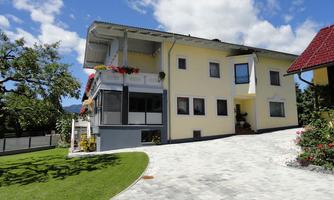 A modern, yellow house with a well-kept driveway. In the foreground, there is a green lawn and a blue sky with some clouds.