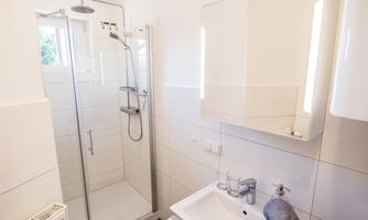 A modern bathroom with a shower and a sink. The walls are light tiled and there is plenty of natural light.
