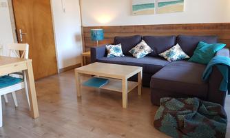 A cozy living area with a dark sofa and decorative cushions. A wooden table and chairs complement the warm atmosphere of the room.