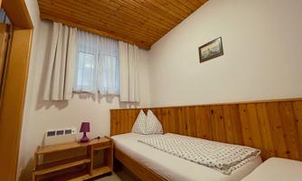 A simple bedroom with two single beds and wooden walls. There is a small lamp and a window with a curtain.
