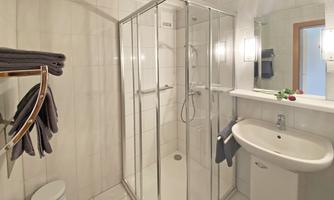 A modern bathroom with a shower cabin and a sink. Towels are neatly hanging next to the shower.
