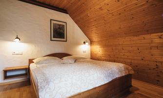A cozy bedroom with a large double bed and a wooden ceiling. A picture hangs on the wall and there are night lights on both sides of the bed.