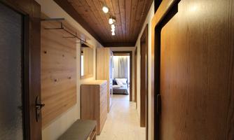 A modern hallway with wood decor and warm lighting. Visible are cabinets, a coat rack, and doors to other rooms.