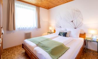 A bright bedroom with two single beds and a window that lets in daylight. There is a decorative pattern on the wall, and the decor is modern and inviting.