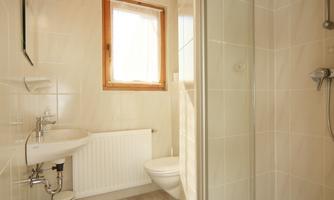 A modern bathroom with a shower cabin and sink. Bright tiles and a window create a friendly atmosphere.