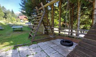 A playground with a seesaw and a tire. In the background, trees and a house are visible.