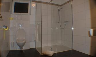 A modern bathroom view with a glass shower cubicle and a toilet. The floor is covered with a colorful bath mat.