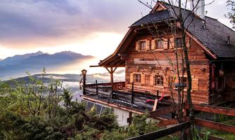 A picturesque wooden cabin in the mountains with a stunning view. In the background, gentle mountains and a dramatic sky scene can be seen.
