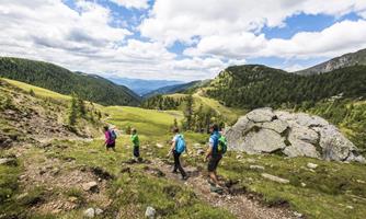 A group of hikers explores a green mountain landscape. The clouds in the sky create a pleasant atmosphere.