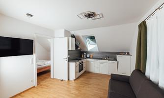 A modern apartment with an open kitchen and seating area. Bright colors and a large window create a pleasant atmosphere.
