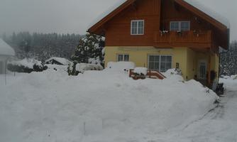 A cozy house with a wooden building, surrounded by deep snow. The landscape is wintry and foggy.