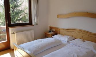 A cozy bedroom with a wooden double bed. The room has a window overlooking greenery and a small nightstand.