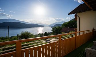 A view from a terrace over a lake with mountains in the background. The sun reflects in the water and the sky is clear.