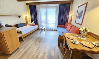 A cozy room with wooden decor, a double bed, and a red sofa. A table with dishes and snacks is also in the room, and the window lets in plenty of daylight.