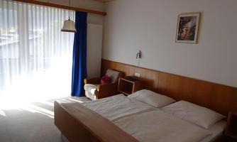 A simple hotel room with a large bed and an armchair. The room has large windows with curtains that let in a lot of light.